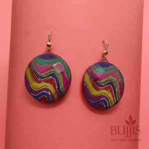 “Colorful handmade polymer clay earrings from Bujjis.in with swirling patterns in green, purple, yellow, blue, and pink on a pink background”